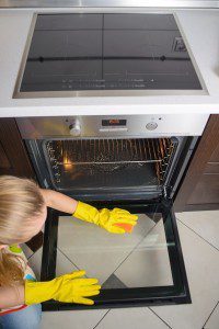 housework and housekeeping concept - close up of woman hand in rubber gloves wiping oven glass door. top view