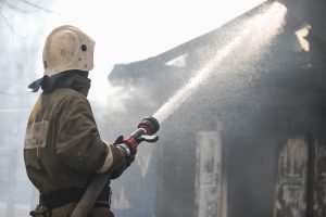 Fireman spraying water in a smouldering burnt out house